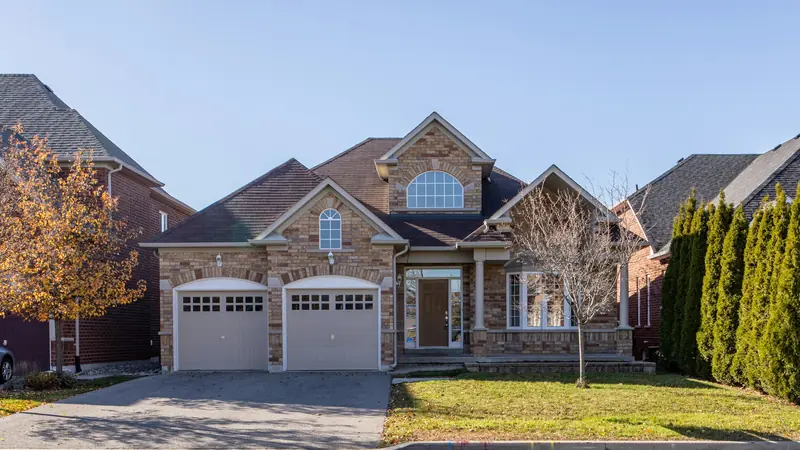 Two-story brick and stone suburban home with a dark asphalt shingle roof under a clear blue sky